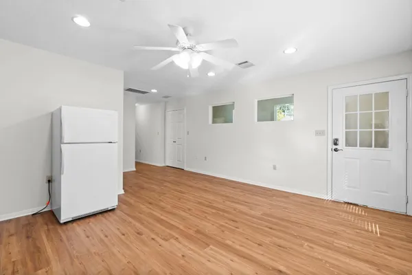 a view of an empty room with wooden floor and a kitchen
