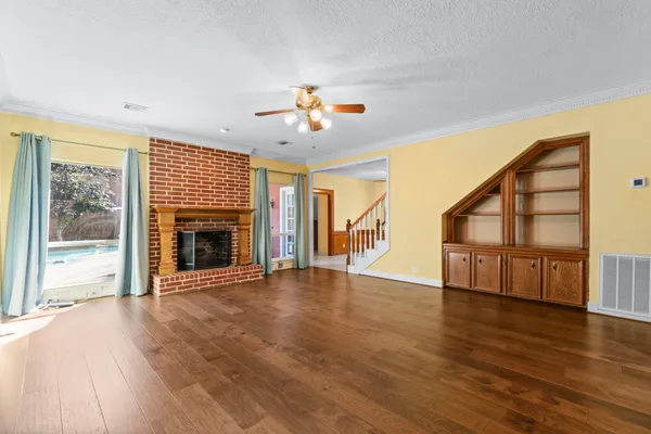 a view of an empty room with wooden floor fireplace and a window