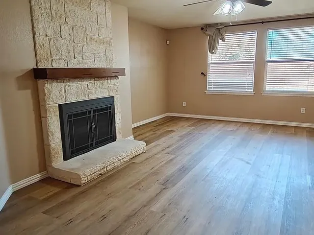 an empty room with wooden floor a fireplace and windows