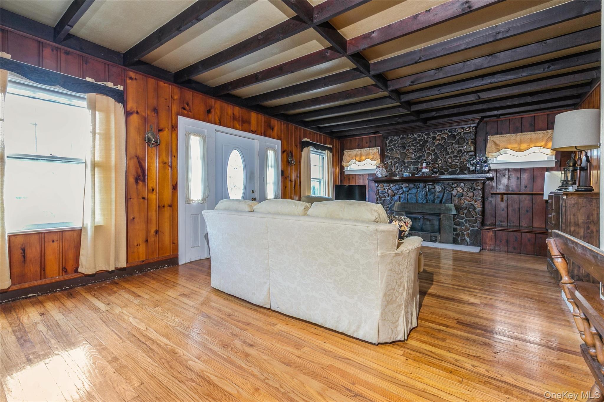 84 Riviera Drive Mastic, NY 11950 - Photo 5 of 28 Living room with wood walls, beam ceiling, light wood-type flooring, and a fireplace