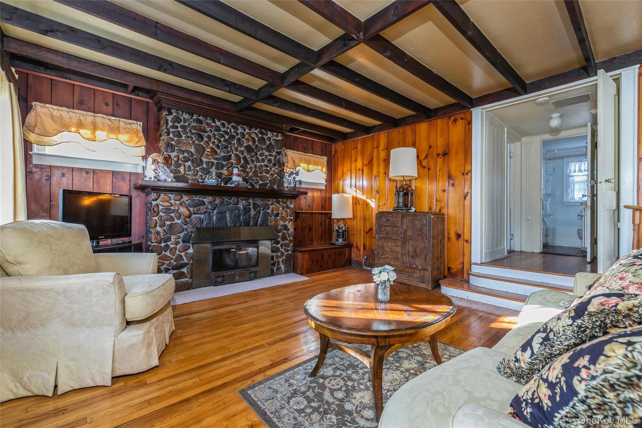 84 Riviera Drive Mastic, NY 11950 - Photo 7 of 28 Living room featuring beamed ceiling, wood walls, wood finished floors, and a fireplace