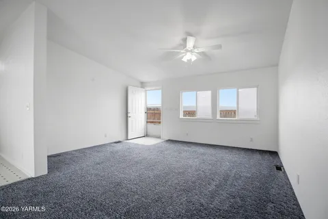 an empty room with chandelier fan and windows
