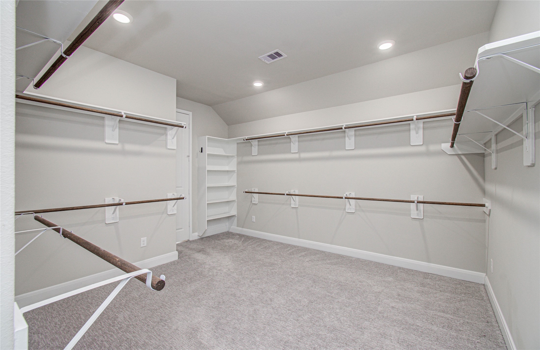 17344 Grand Canyon Road Conroe, TX 77302 - Photo 29 of 49 This is a spacious walk-in closet with ample hanging space on multiple rods and built-in corner shelving, featuring soft carpeted flooring and recessed lighting for a modern touch.
