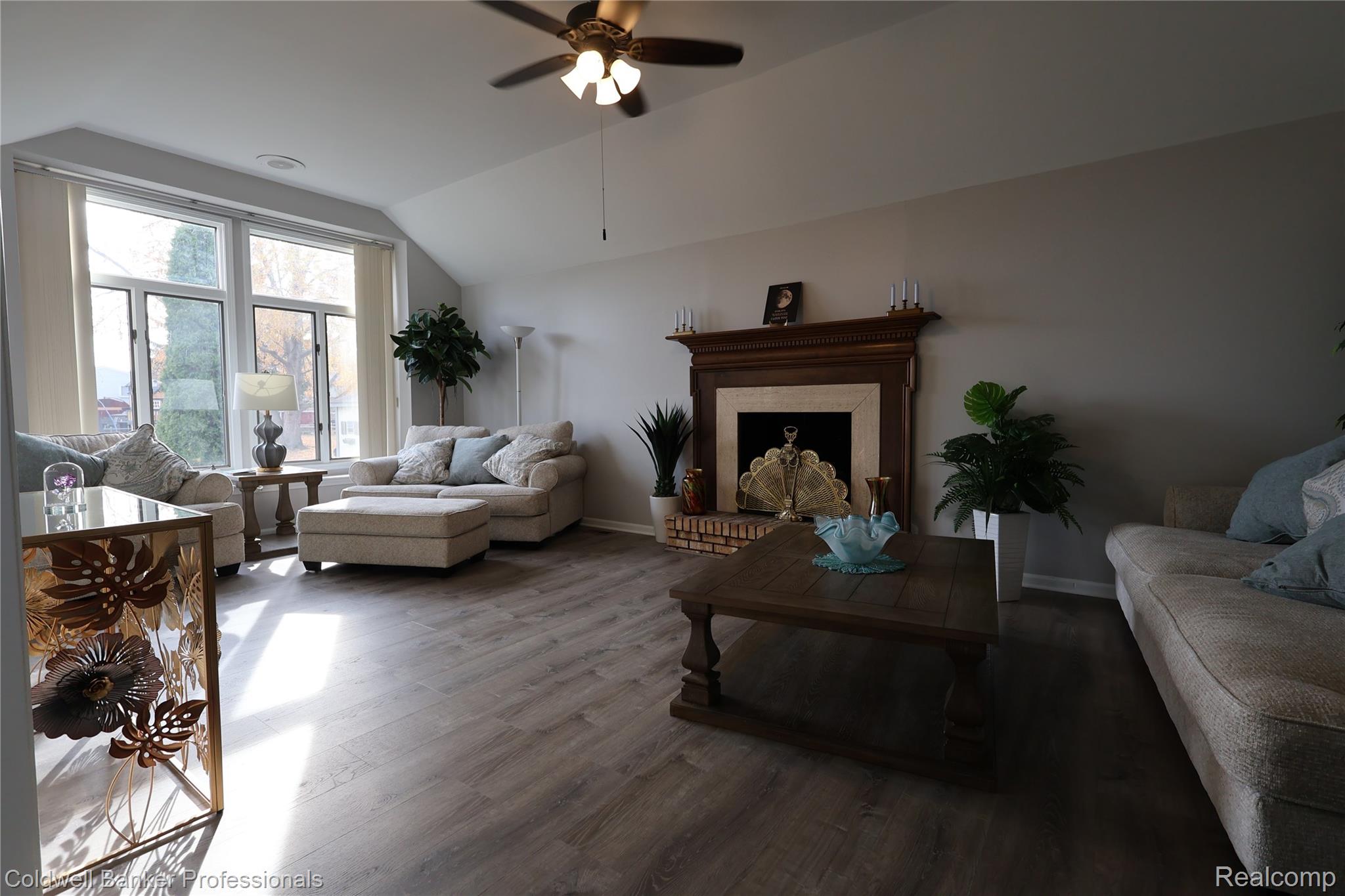 Living area with lofted ceiling, wood finished floors, a brick fireplace, and a ceiling fan