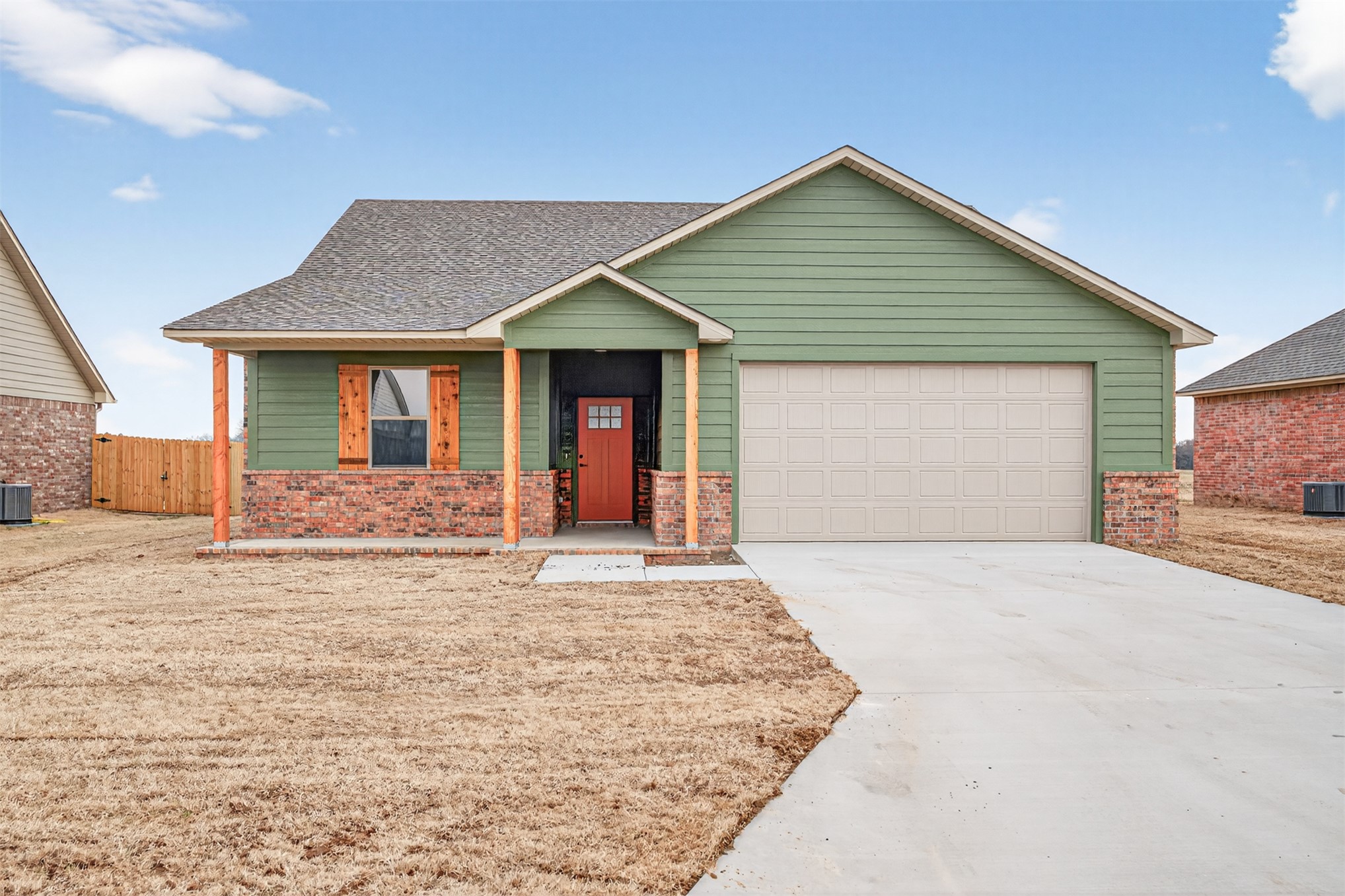 124 Countryside Way Pocola, OK 74902 - Photo 1 of 39 Siding exterior with brick accents, covered front entry, wooden porch columns, a contrasting red front door, and an attached garage with a concrete driveway