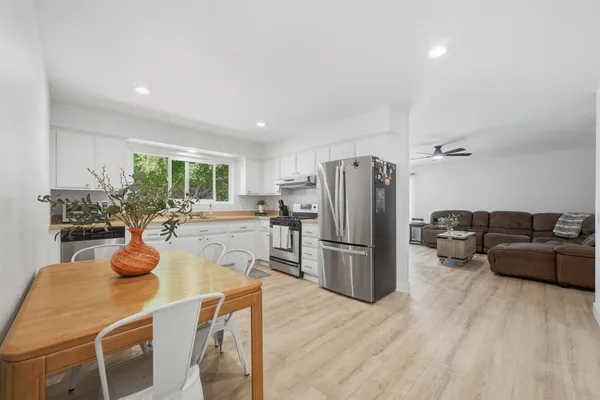 a kitchen with stainless steel appliances a refrigerator a sink dishwasher a dining table and chairs with wooden floor