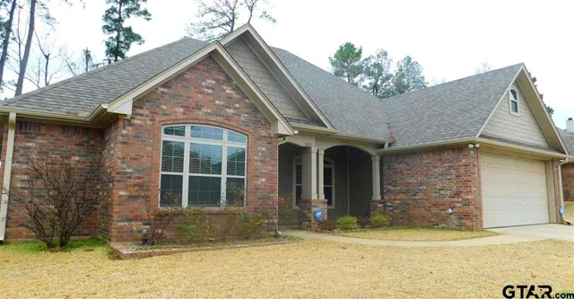 a view of a house with small yard plants and large tree