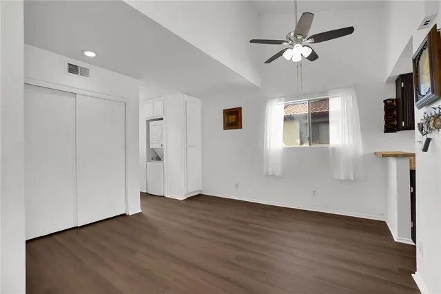 a view of an empty room with wooden floor and a ceiling fan