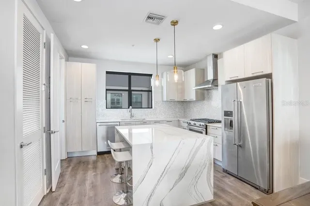 a kitchen with stainless steel appliances granite countertop a refrigerator a sink and wooden floors