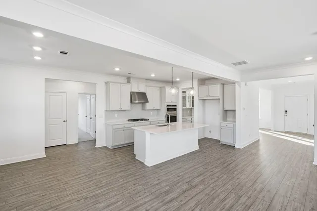 a large white kitchen with kitchen island a sink wooden floor and stainless steel appliances
