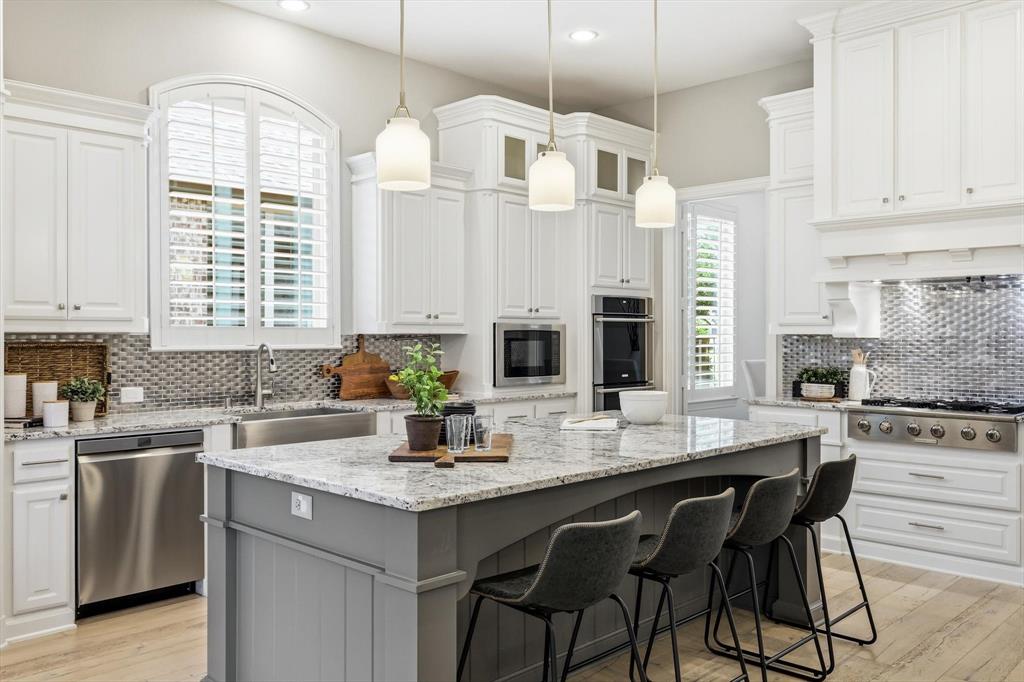 1933 Snapdragon Road Frisco, TX 75033 - Photo 7 of 40 Expansive kitchen featuring white cabinetry, a center island with gray paneling, stainless steel appliances, and a mosaic tile backsplash