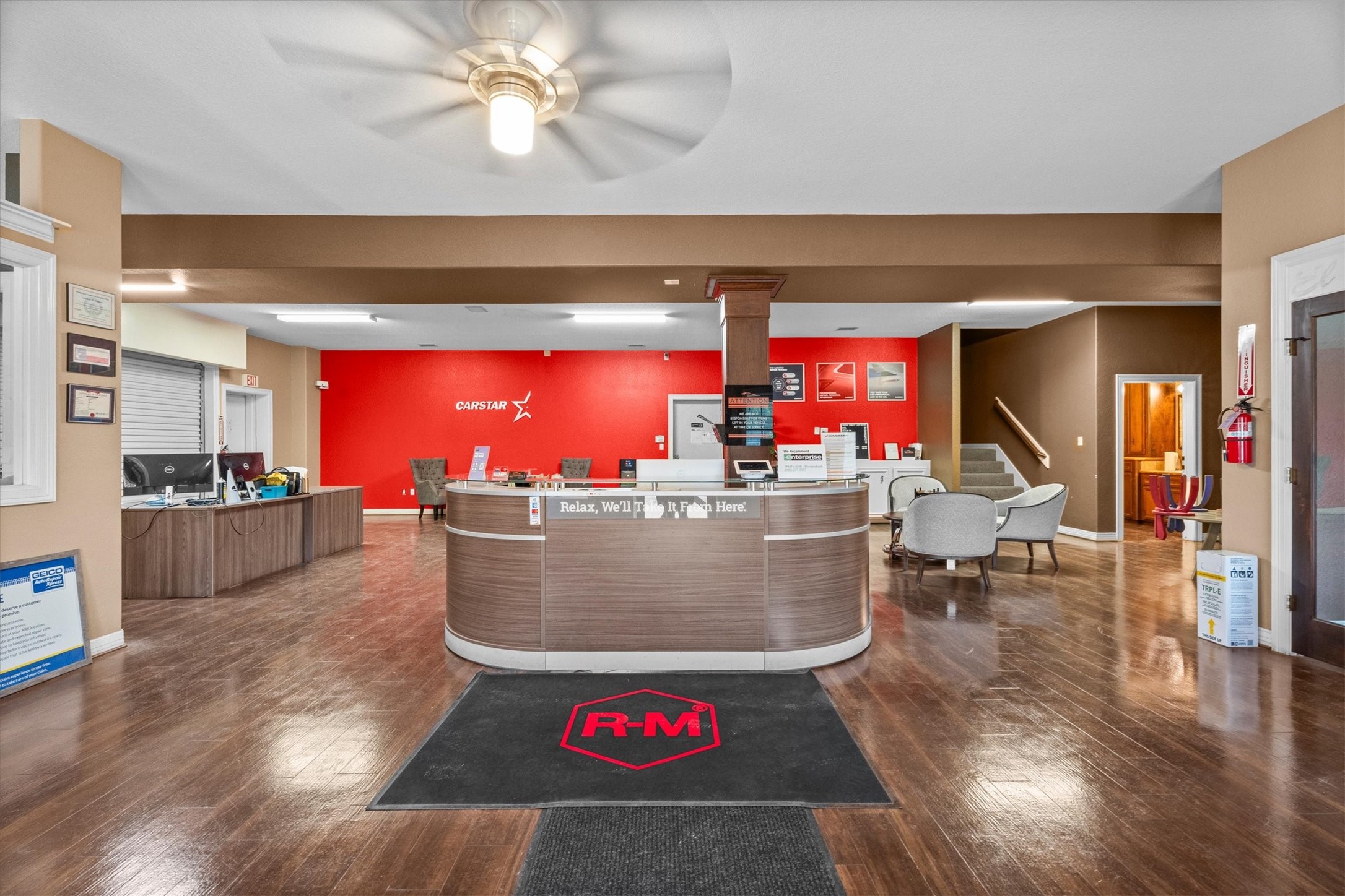 11066 Sh 242 Conroe, TX 77385 - Photo 8 of 21 This photo shows a spacious commercial reception area with modern furnishings, a central curved desk, and hardwood floors. The space is well-lit and welcoming, featuring a red accent wall and comfortable seating.