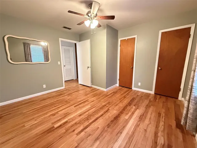 a view of an empty room with wooden floor and a ceiling fan