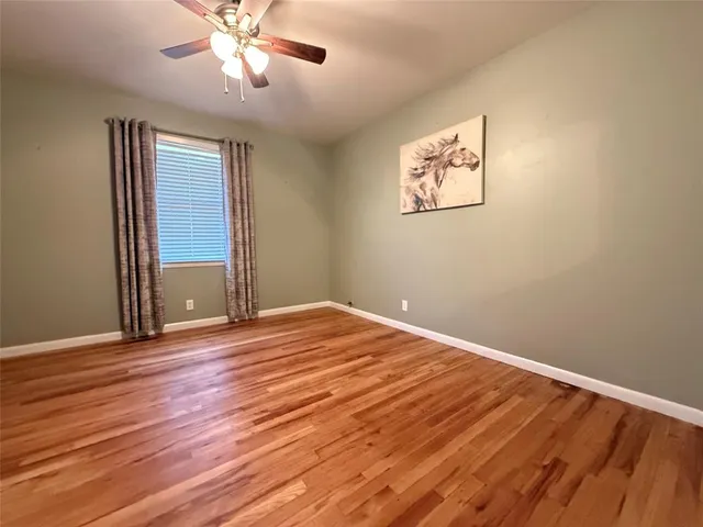 a view of an empty room with wooden floor and a ceiling fan