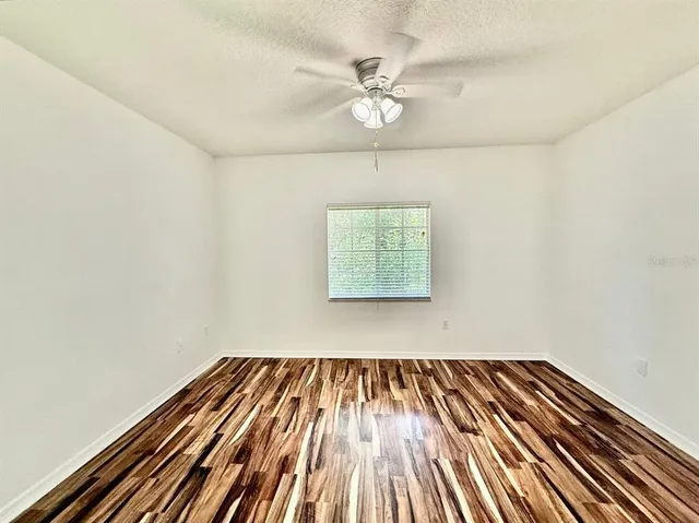 an empty room with wooden floor chandelier fan and windows