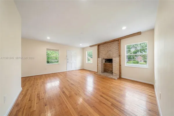 an empty room with wooden floor fireplace and windows