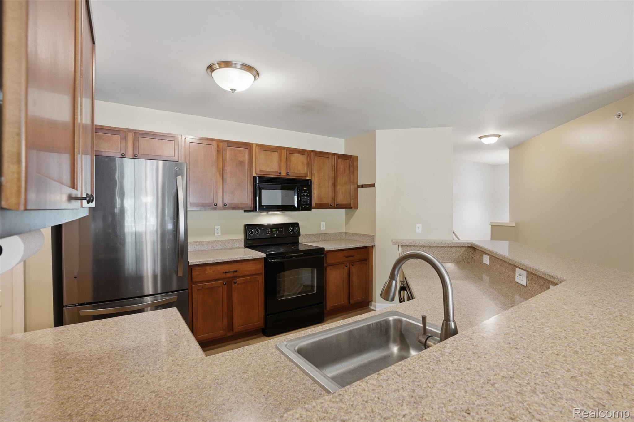 320 North Wixom Road, Unit 30 Wixom, MI 48393 - Photo 15 of 28 Kitchen featuring light wood cabinetry, stone-look countertops, stainless steel appliances, a stainless steel sink with a high-arch faucet, and a breakfast bar