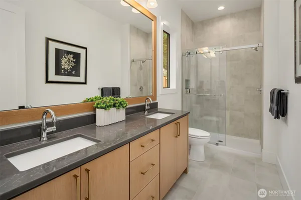 a spacious bathroom with a granite countertop sink a toilet a mirror a vanity and shower