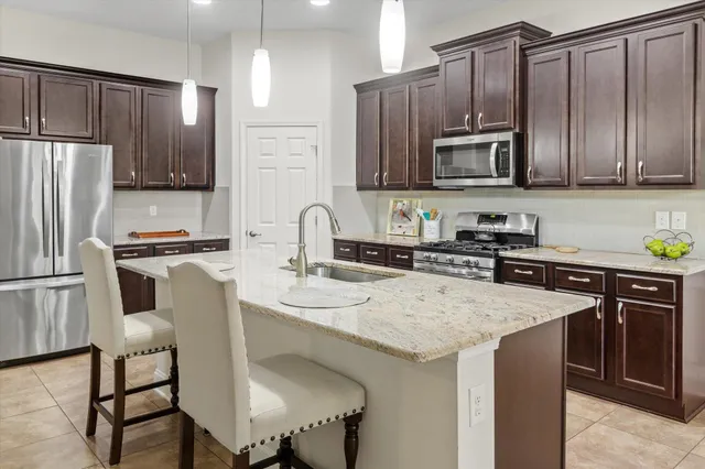 a kitchen with granite countertop stainless steel appliances a sink a stove top oven a refrigerator cabinets and a sink