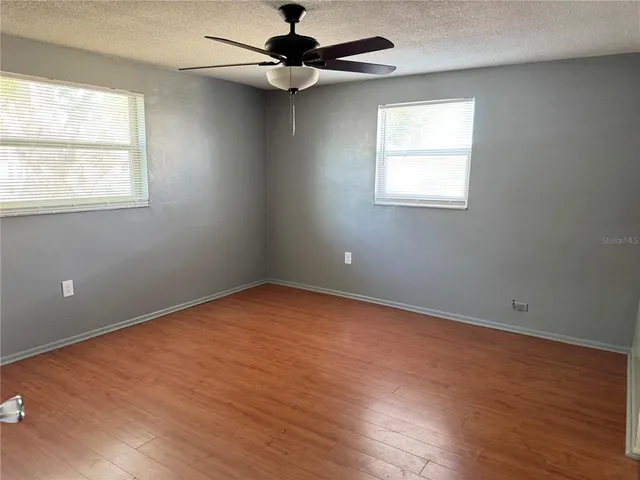 an empty room with wooden floor ceiling fan and windows