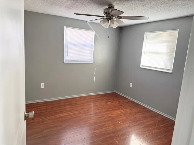an empty room with wooden floor fan and windows