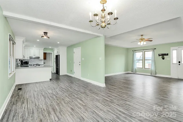 a view of an empty room and kitchen with wooden floor