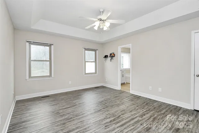 an empty room with wooden floor chandelier fan and windows