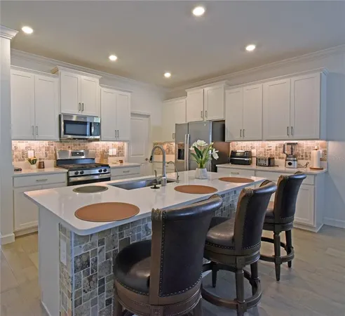 a kitchen with kitchen island granite countertop a sink a stove a refrigerator cabinets and chairs