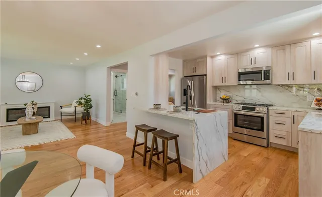 a kitchen with stainless steel appliances kitchen island granite countertop a stove a sink a refrigerator and white cabinets with wooden floor