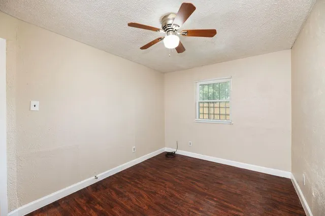 an empty room with wooden floor ceiling fan and window