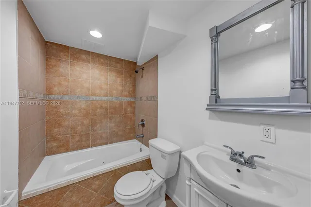 a bathroom with a bathtub shower sink vanity mirror and toilet