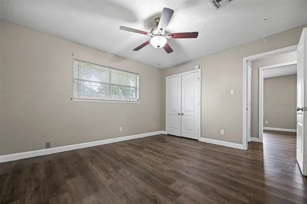 a view of an empty room with wooden floor and a ceiling fan