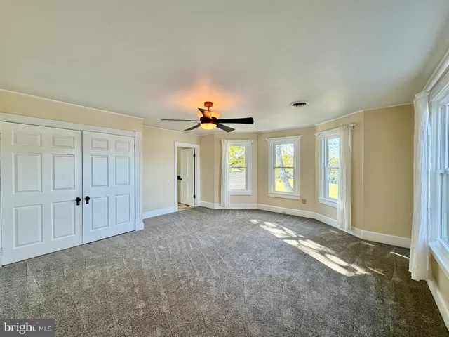 a view of an empty room with chandelier fan and windows