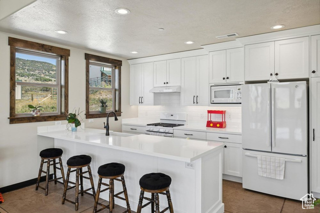 6117 North Rocky Ridge Road Peoa, UT 84061 - Photo 17 of 83 Kitchen featuring a kitchen bar, kitchen peninsula, white cabinets, white appliances, and backsplash