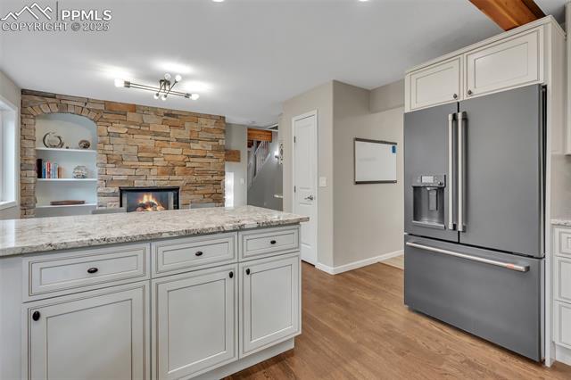 615 Cimarron Road Monument, CO 80132 - Photo 15 of 50 Kitchen featuring high quality fridge, a stone fireplace, light wood-style flooring, white cabinets, and light stone countertops