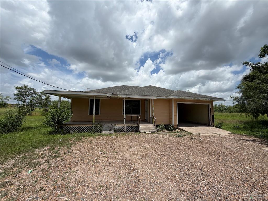 Single-story residence featuring a covered front porch, an integrated carport, and a gravel driveway