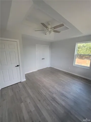 an empty room with wooden floor ceiling fan and windows