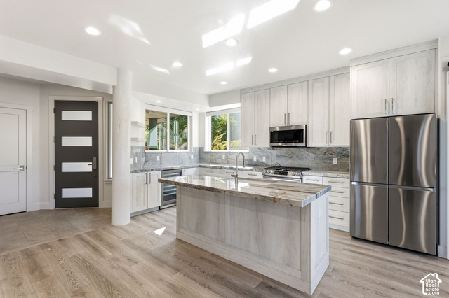 Gourmet kitchen with stainless steel appliances, light wood-finish cabinetry, and a center island with a stone countertop