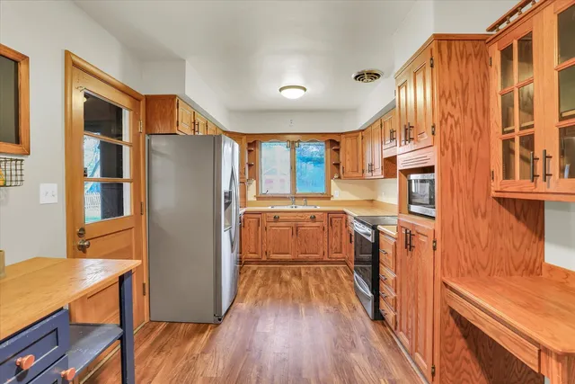 a kitchen with stainless steel appliances granite countertop a refrigerator a sink dishwasher a stove and a dining table with wooden floor