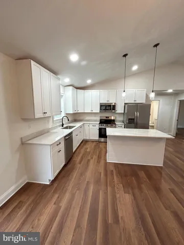 a large kitchen with stainless steel appliances granite countertop a stove a sink dishwasher a refrigerator and white cabinets with wooden floor