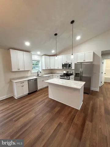 a large kitchen with kitchen island a stove a sink dishwasher a refrigerator and white cabinets with wooden floor