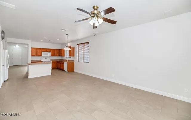 a view of an empty room with a ceiling fan and kitchen view