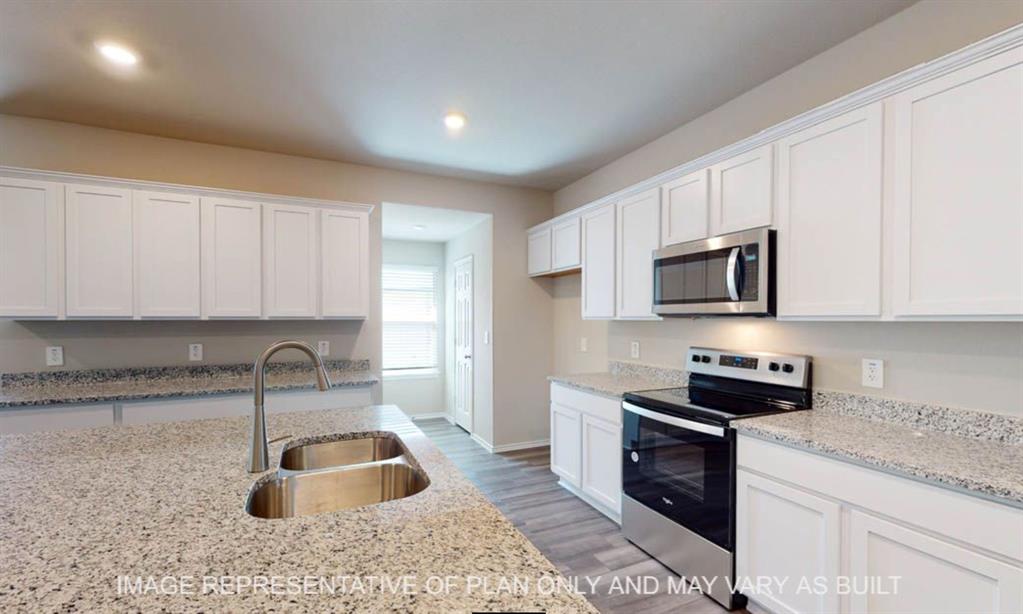 10204 Neptune Court Waco, TX 76708 - Photo 4 of 20 Spacious kitchen featuring an expansive island with an undermount double basin stainless steel sink, white shaker cabinetry, stainless steel appliances, speckled stone countertops, and wood-finish flooring
