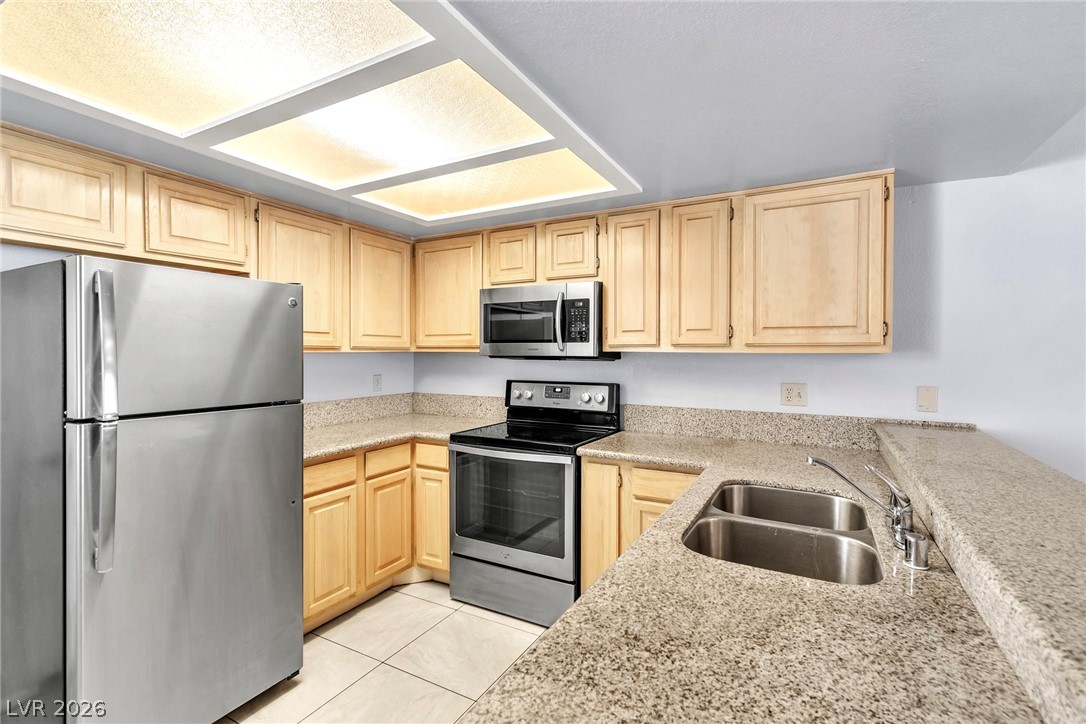 6250 West Flamingo Road, Unit 98 Las Vegas, NV 89103 - Photo 7 of 40 Kitchen featuring light tile patterned flooring, light stone counters, a sink, light brown cabinetry, and stainless steel appliances