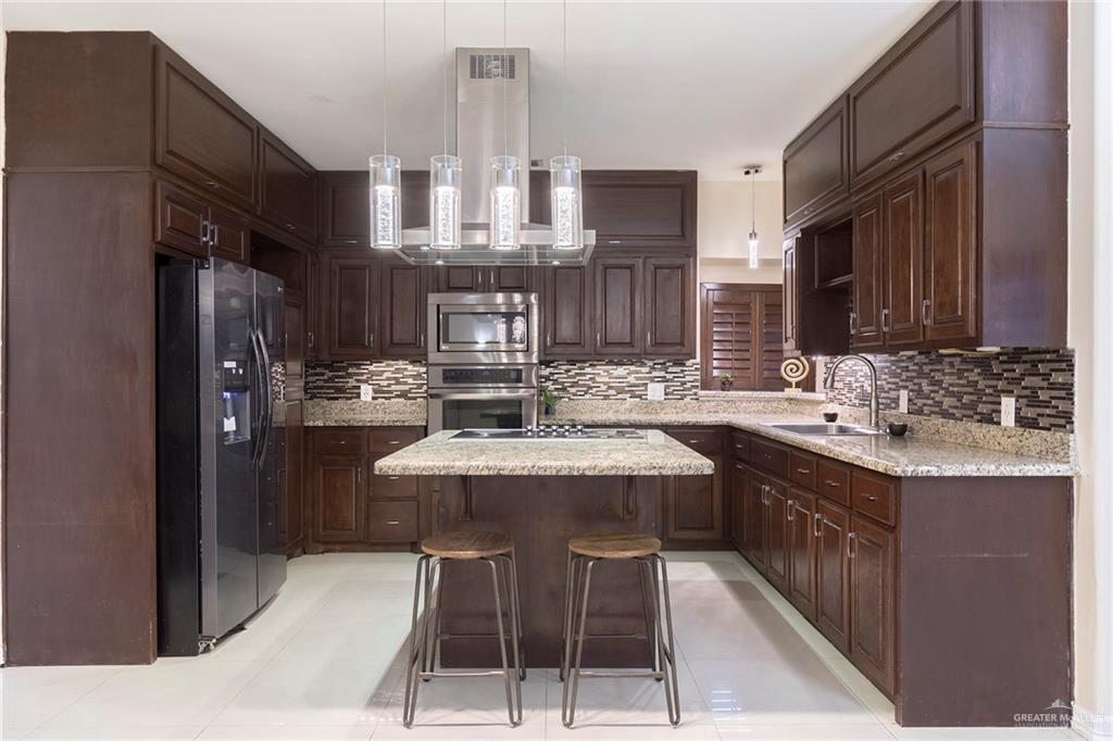 2001 Quail Lane Mission, TX 78572 - Photo 6 of 28 Kitchen featuring dark wood cabinetry, light granite countertops, stainless steel appliances, and a tiled backsplash