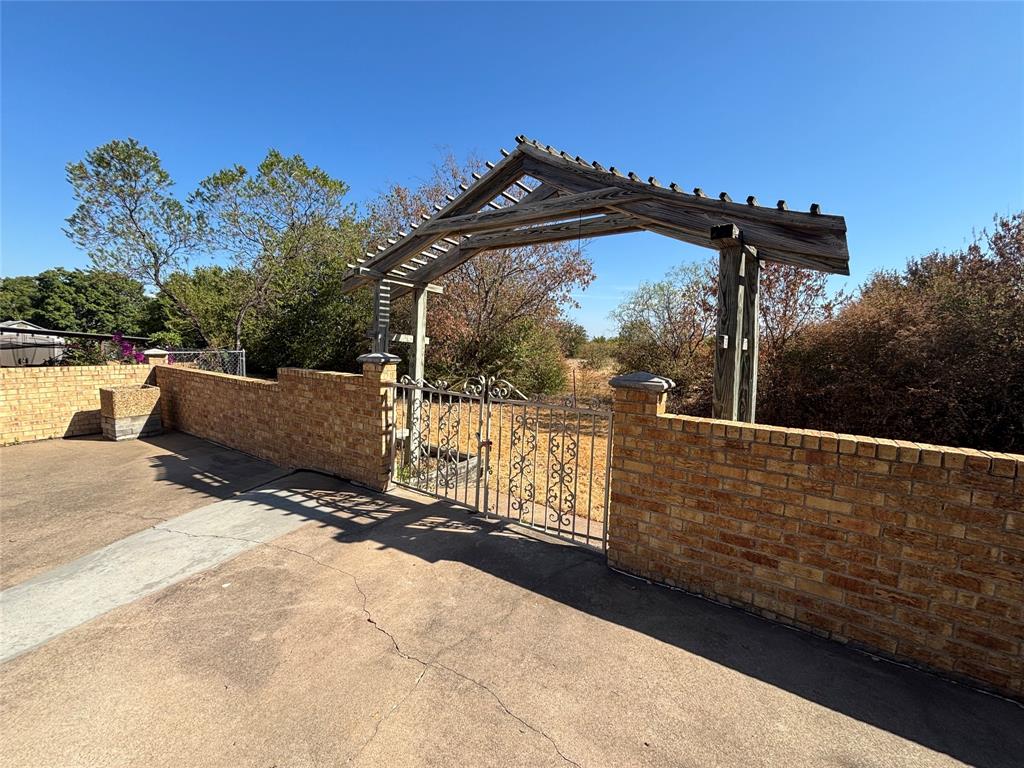 4702 Ranch View Road Fort Worth, TX 76109 - Photo 31 of 40 Brick wall with capstone detail, wrought iron gate, and a wood pergola entry