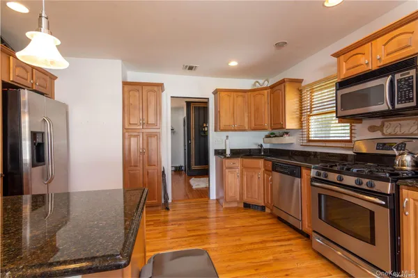 a kitchen with stainless steel appliances granite countertop a stove top oven a sink dishwasher a refrigerator and cabinets with wooden floor