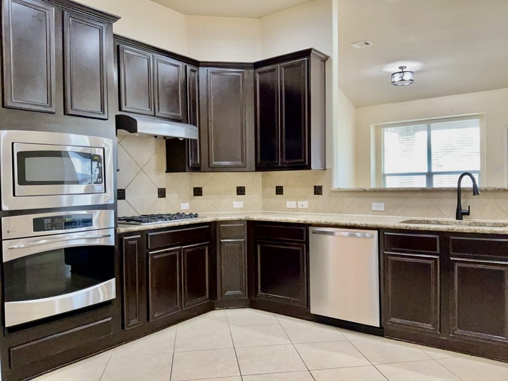 2946 Todd Trail Round Rock, TX 78665 - Photo 6 of 31 Kitchen featuring stainless steel appliances, dark wood finish cabinetry, backsplash, light stone countertops, and light tile patterned floors