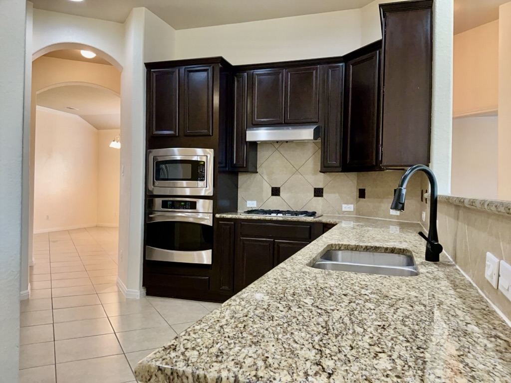 2946 Todd Trail Round Rock, TX 78665 - Photo 7 of 31 Kitchen with arched walkways, light stone countertops, stainless steel appliances, and backsplash