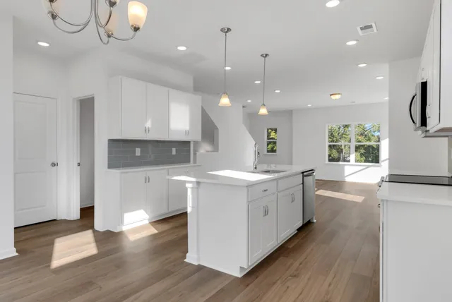 a large kitchen with white cabinets a sink dishwasher a dining table and chairs with wooden floor